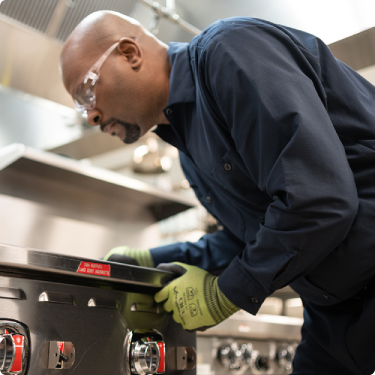 ESI technician bending over the control knobs of a commercial range to diagnose a problem