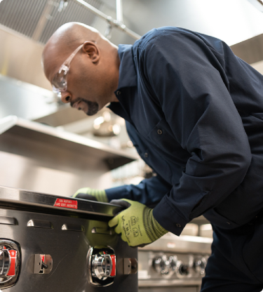 ESI technician bending over the control knobs of a commercial range to diagnose a problem