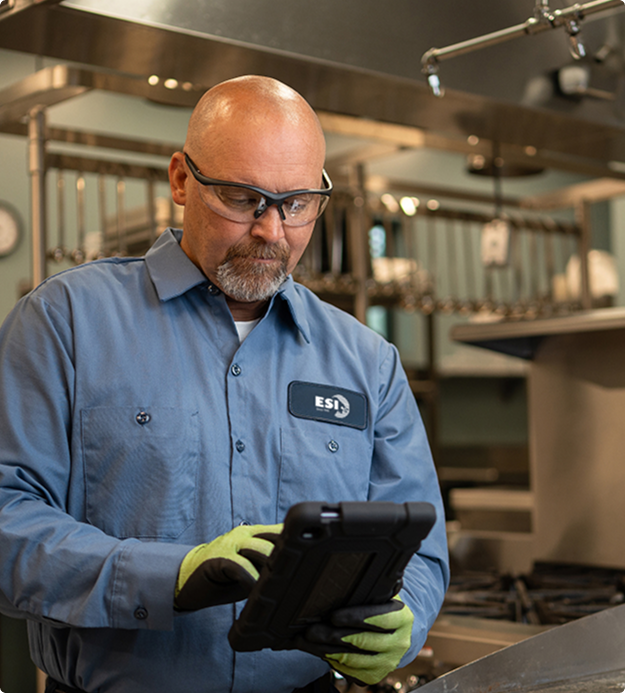 ESI technician in a branded work shirt using a tablet to log a service visit in a commercial kitchen