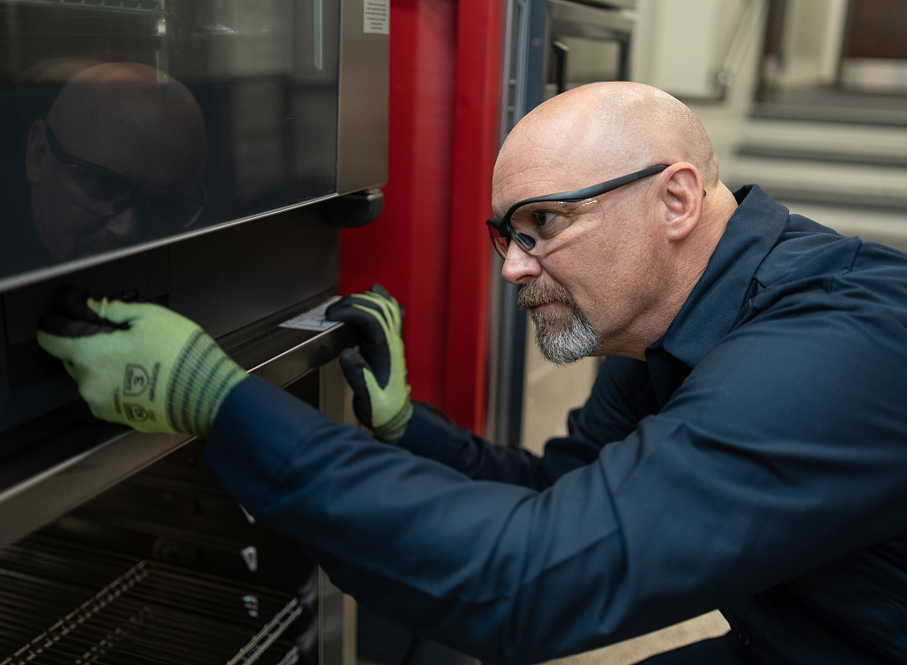 ESI technician in safety glasses and cut-resistant gloves opening the door of a commercial oven