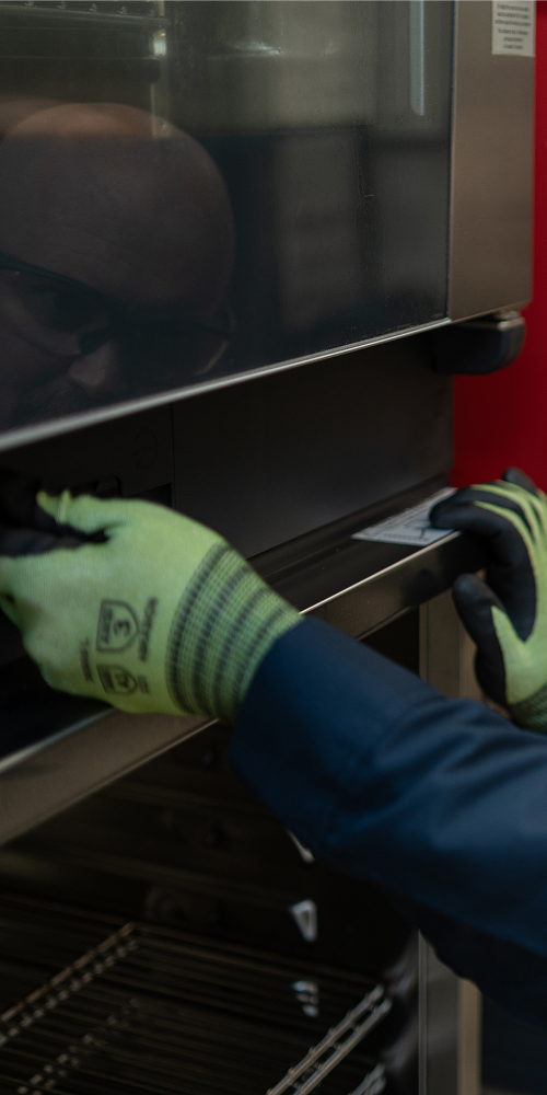 ESI technician in safety glasses and cut-resistant gloves opening the door of a commercial oven
