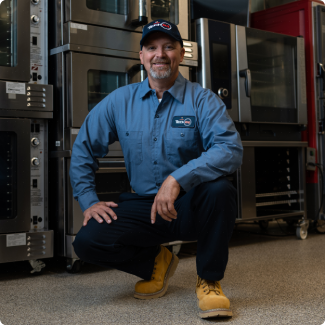 Smiling ESI service technician in uniform kneeling in front of a bank of commercial combi ovens
