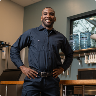 Smiling ESI service technician in uniform standing with hands on hips in a commercial kitchen