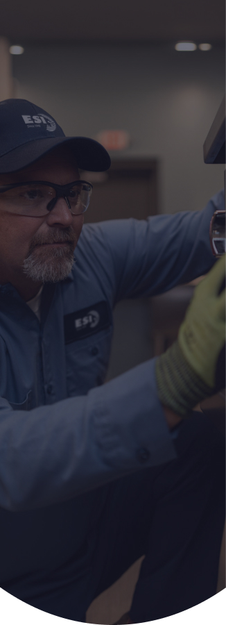 ESI technician in a branded cap and safety glasses reaching into the burner assembly of a piece of commercial cooking equipment